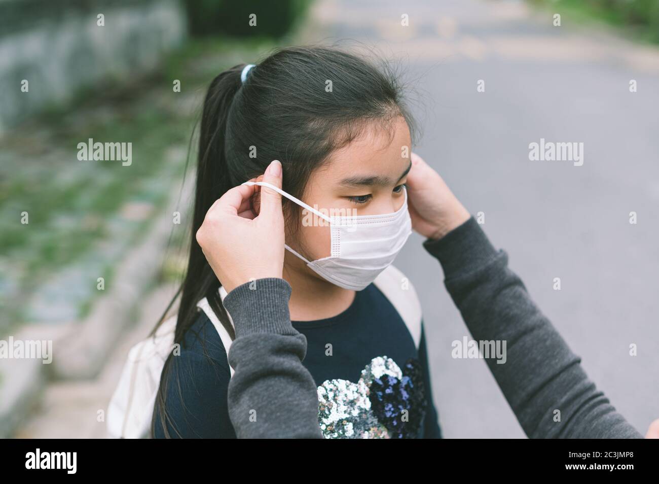 Mutter legt eine Sicherheitsmaske auf Tochter Gesicht zum Schutz Covid-19 oder Coronavirus Ausbruch im Dorfpark vorzubereiten gehen zur Schule. Zurück zur Schule con Stockfoto