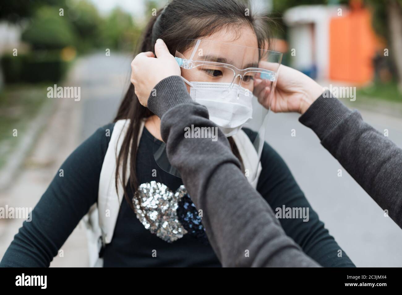 Mutter legt eine Sicherheitsmaske auf Tochter Gesicht zum Schutz Covid-19 oder Coronavirus Ausbruch im Dorfpark vorzubereiten gehen zur Schule. Zurück zur Schule con Stockfoto