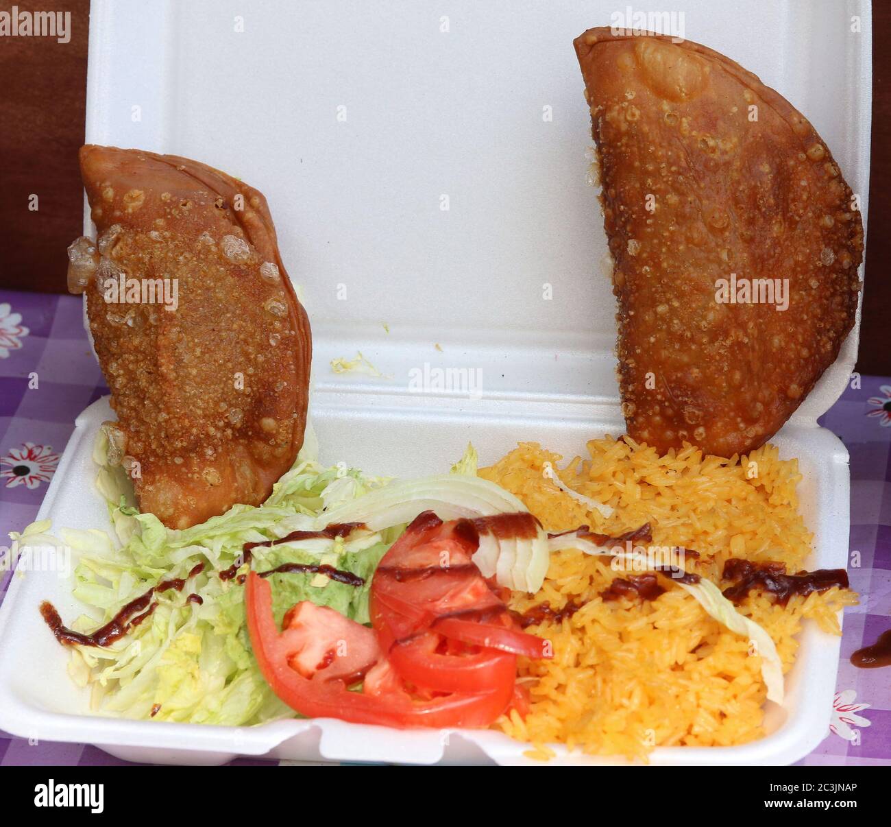 Käse und Fleisch Empanadas mit Salat, Tomaten, gelbem Reis und Sauce auf Styropor Lebensmittelbehälter Stockfoto