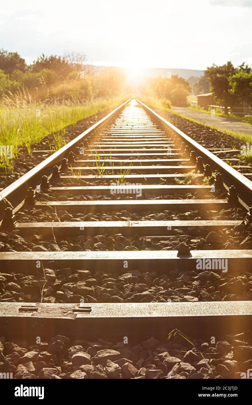 Endlose Bahngleise zwischen grünen Feldern im Sonnenlicht Stockfoto