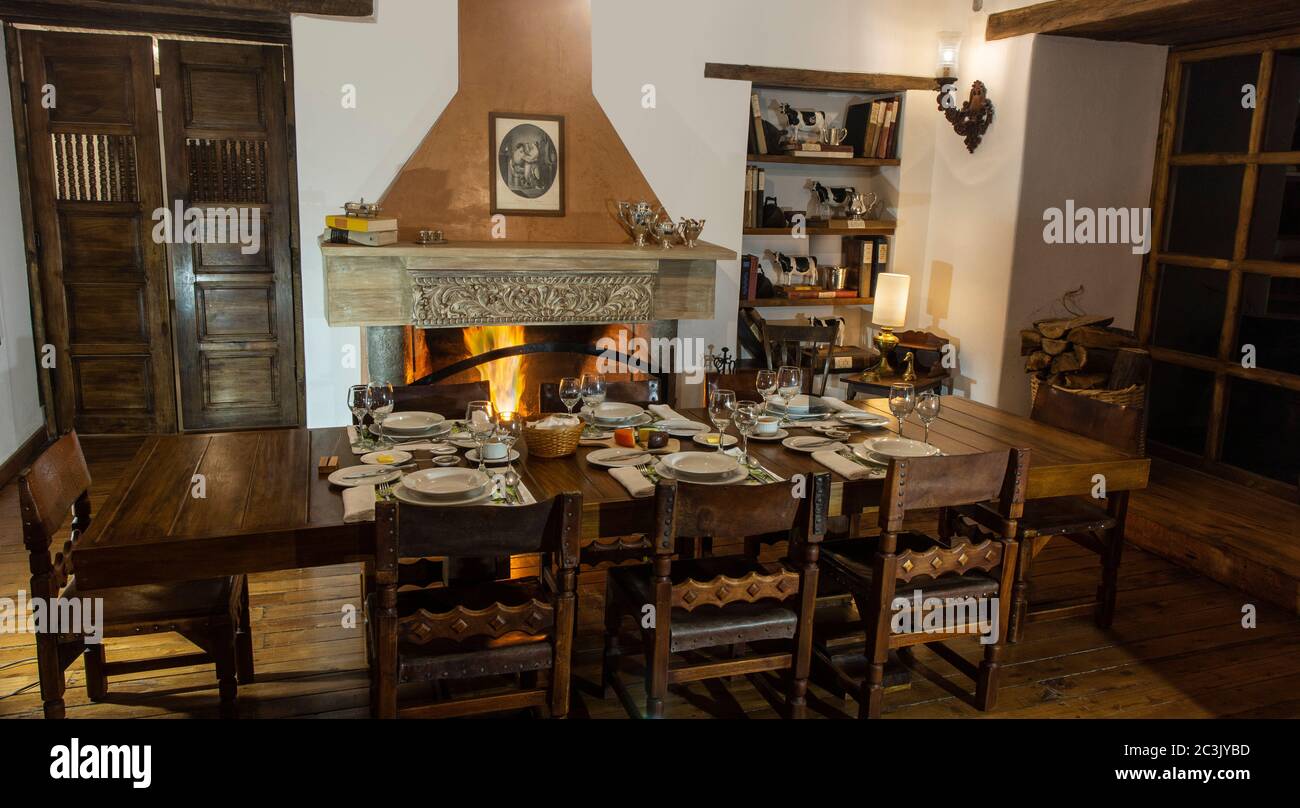 Zuleta, Imbabura / Ecuador - 8. November 2018: Blick auf ein Esszimmer eines alten Hauses mit Holztisch serviert und mit dem Kamin beleuchtet Stockfoto