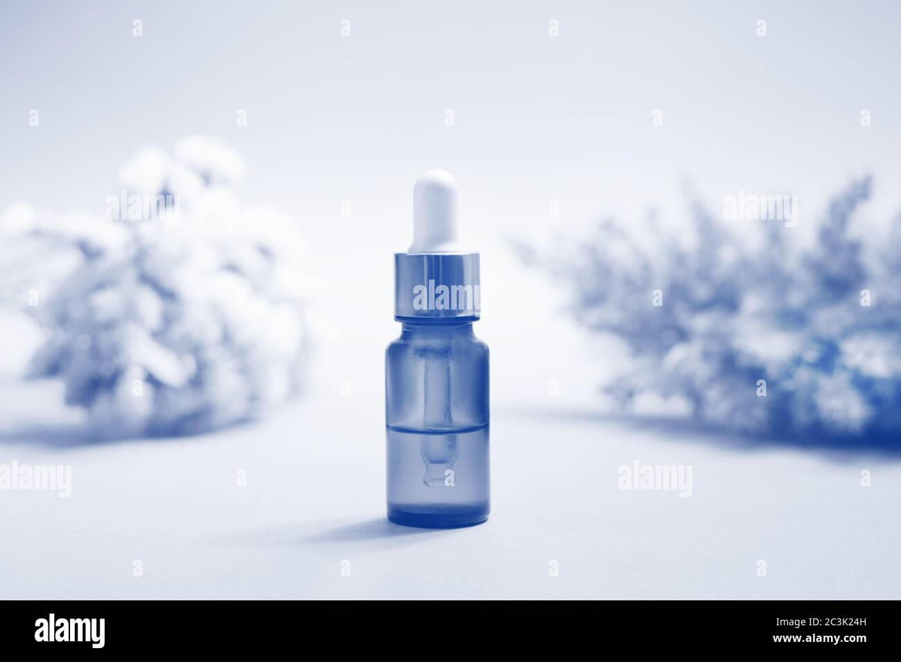 Eine Glasflasche mit Pipette mit weißer Gummispitze zwischen vielen schönen Blumen auf dem blauen Hintergrund. Naturhautkonzept. Bio-Spa C Stockfoto