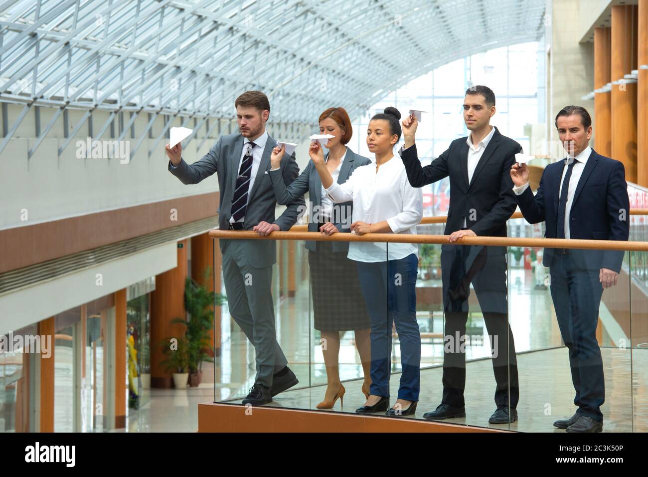 Team von Geschäftsleuten, die Papierflugzeuge in einem modernen Bürogebäude zusammenwerfen Stockfoto