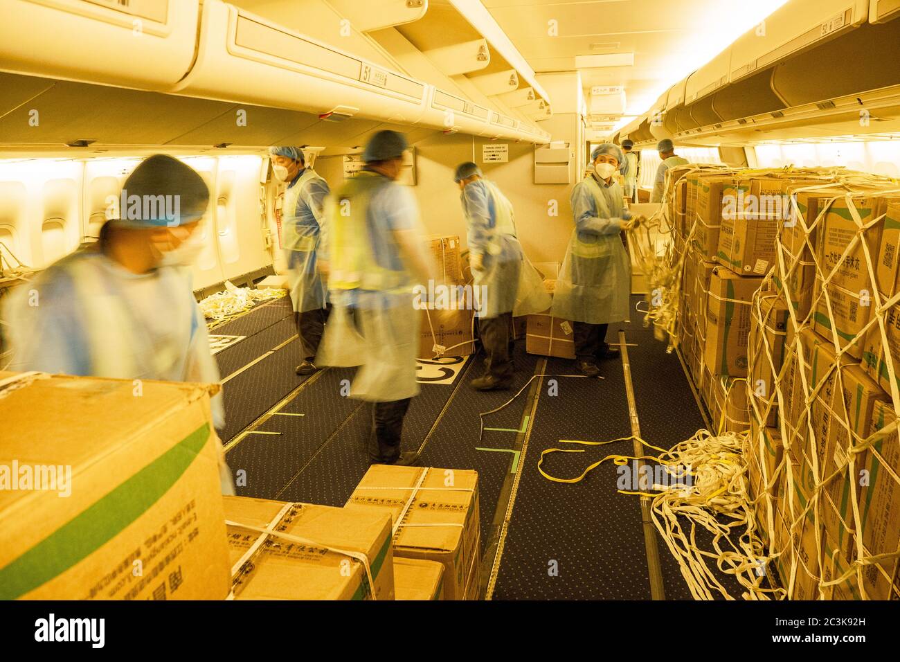 Chinesische Lader tragen Hazmat Anzüge Laden eines umgebauten Fahrgastes in Frachtschiff Flugzeug mit chirurgischen Masken und Kleider zu kämpfen COVID-Pandemie Stockfoto