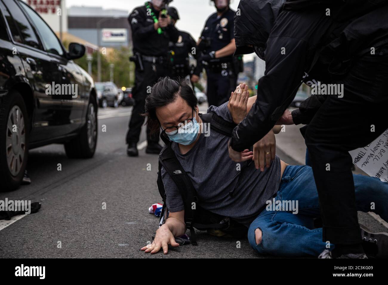 Ein Protestant in Los Angeles wird nach dem Schiebe auf den Boden von einem Offizier geholfen. Man sieht einen Offizier, der mit einer nicht-tödlichen Waffe auf ihn zielt. Stockfoto