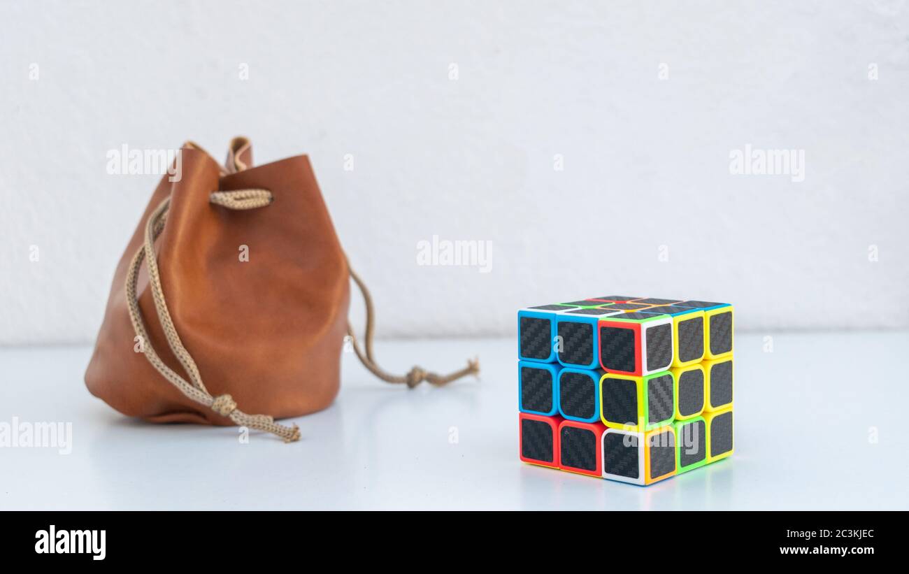 Nahaufnahme eines unvollendeten Rubik's Cube neben einem Ledertasche auf einer weißen Oberfläche und Hintergrund Stockfoto