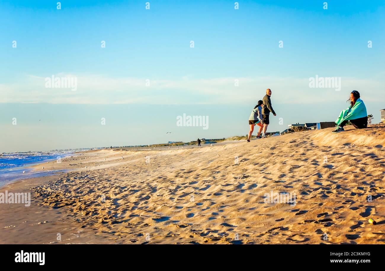 Ein Tourist sitzt am Strand bei Sonnenaufgang, in Gedanken verloren, wie andere lachen und spielen, 21. März 2016, in St. Augustine, Florida. Stockfoto