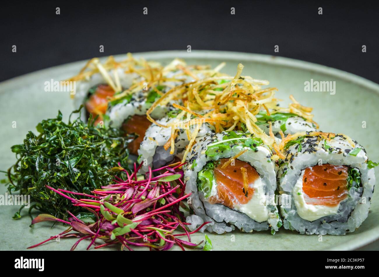 Sushi, traditionelle japanische Küche. Leckeres Uramaki auf dekorierten Teller, schwarzer Hintergrund. Stockfoto
