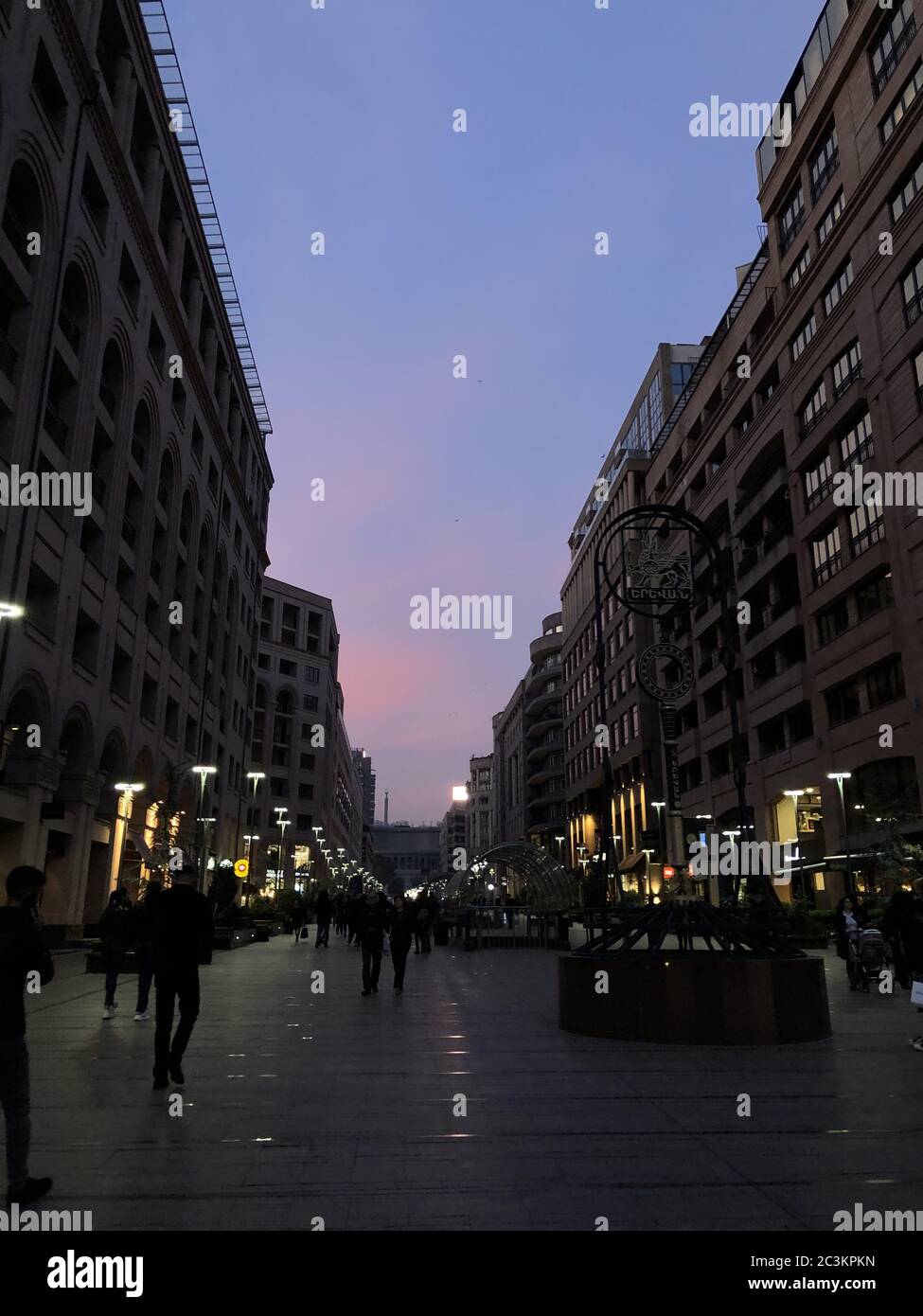 Vertikale Aufnahme von Menschen, die während des Sonnenuntergangs in der nördlichen Allee von Jerewan, Armenien, spazieren gehen Stockfoto