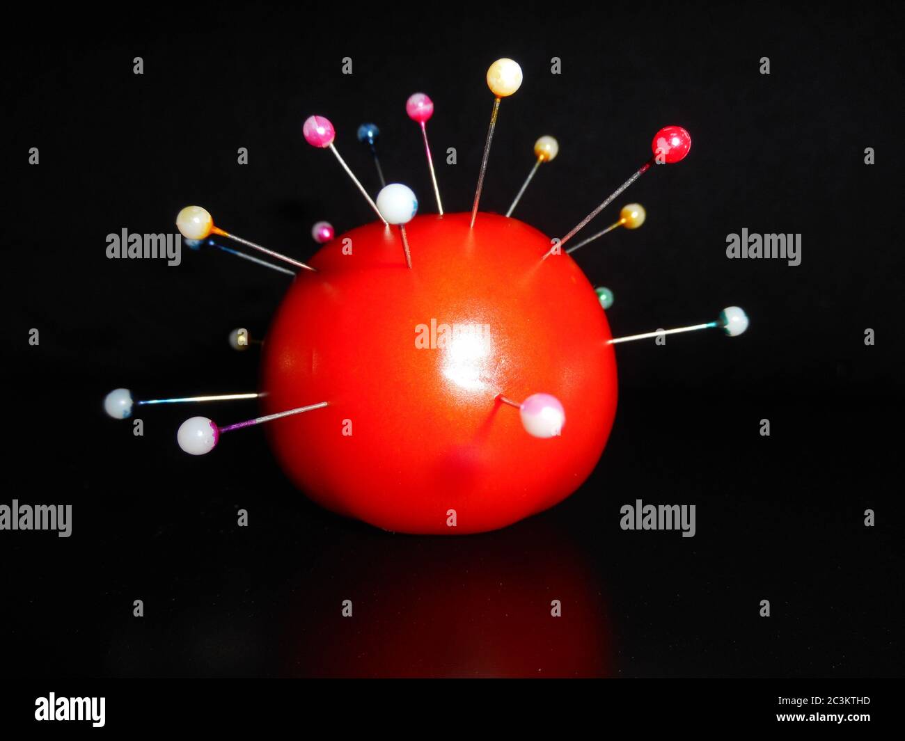 Farbige Stifte sind auf Tomate, über schwarzem Hintergrund, Konzept der Corona-Virus-Form durchdrungen. Stockfoto