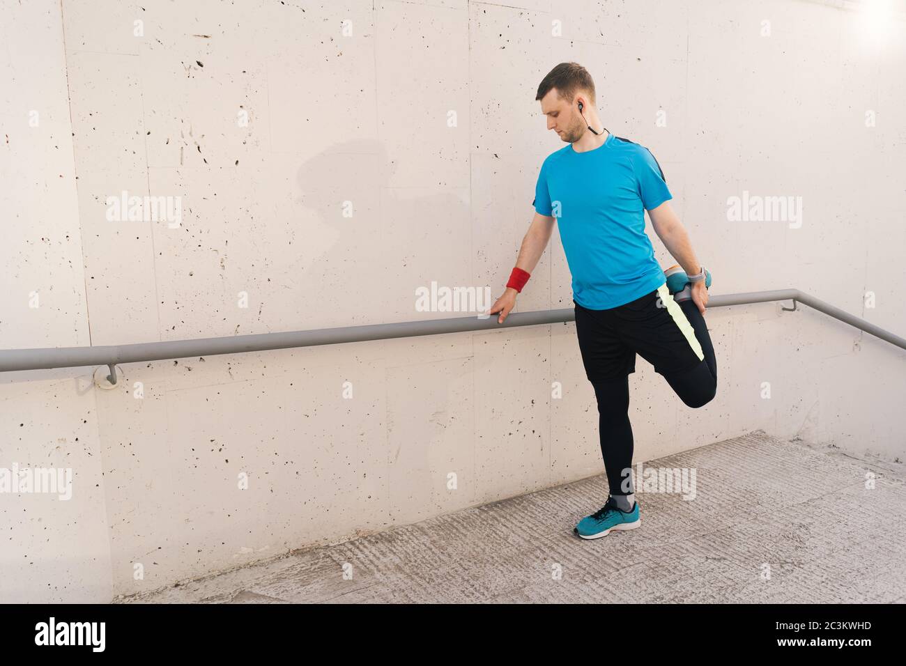 Junger Mann Läufer immer bereit zu laufen Stretching Beine wärmen Quad Stretch Übung auf Außentreppe Stockfoto