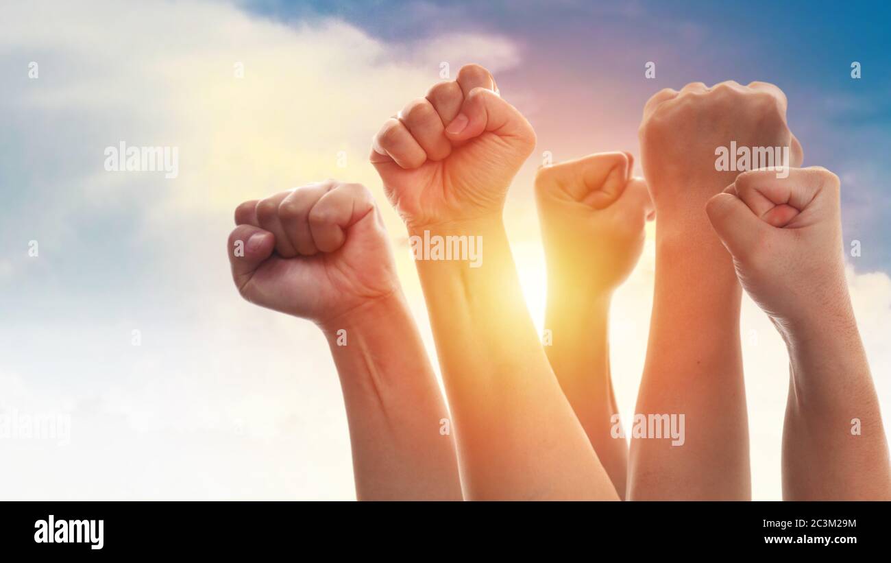 Aufgehende Faust von erwachsenen Menschen, männlich und weiblich, über dramatischen blauen Himmel mit Sonnenlicht, Wut Protest Revolution Inspiration Motivation oder Teamwork conce Stockfoto