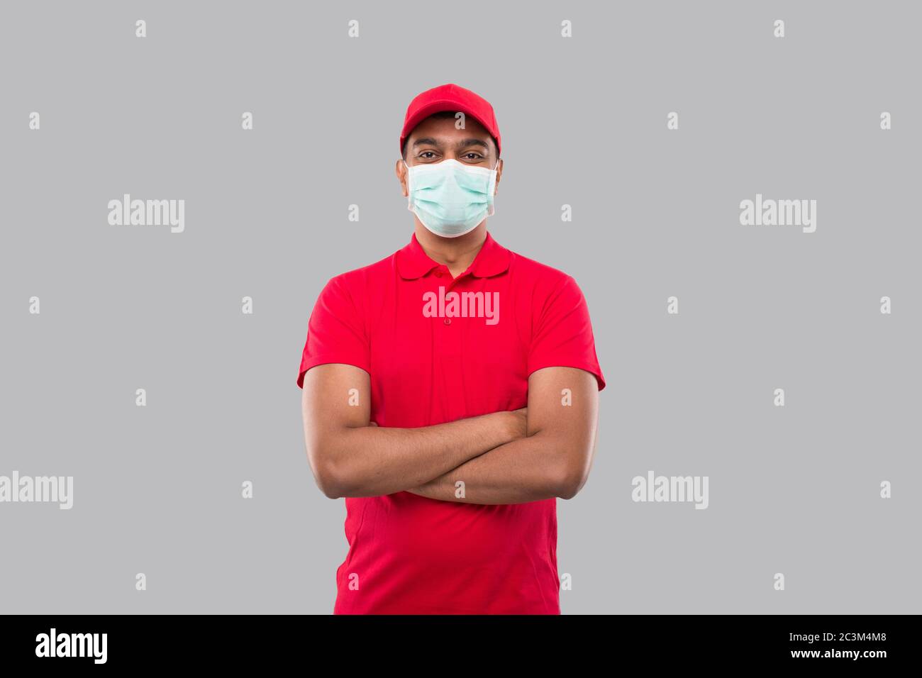 Lieferung Mann Stehende Hände Gekreuzt Tragen Medizinische Maske Isoliert. Indische Lieferung Junge in rot Uniform Stockfoto