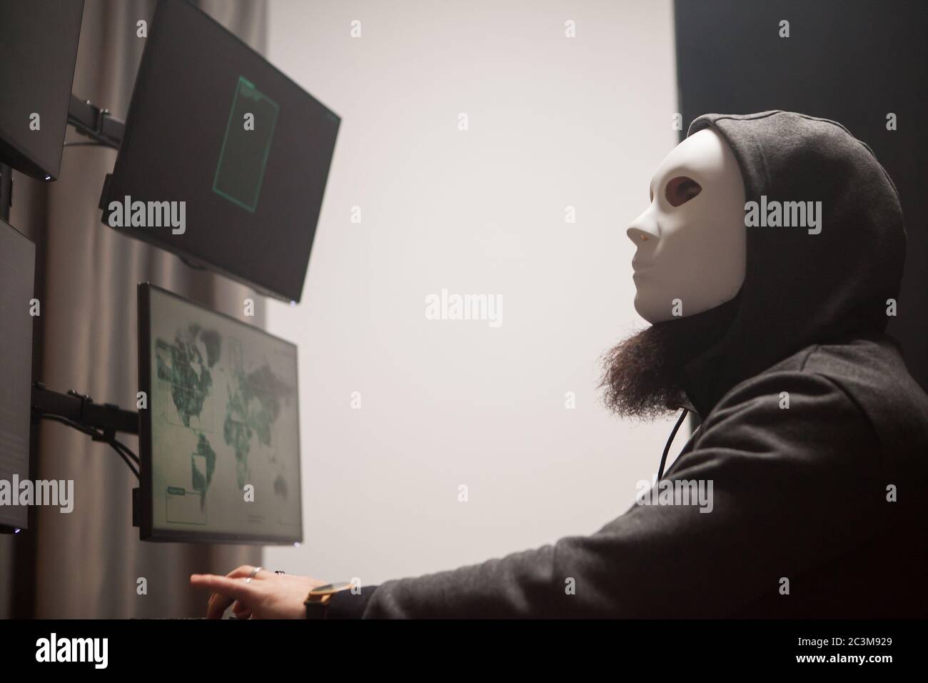 Seitenansicht von maskierten und gefährlichen Hacker mit Computer mit mehreren Bildschirmen. Stockfoto