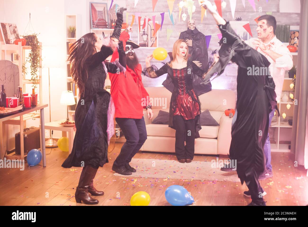 Gruppe von Freunden tanzen mit den Händen nach oben, während Halloween in ihren Kostümen feiern. Stockfoto