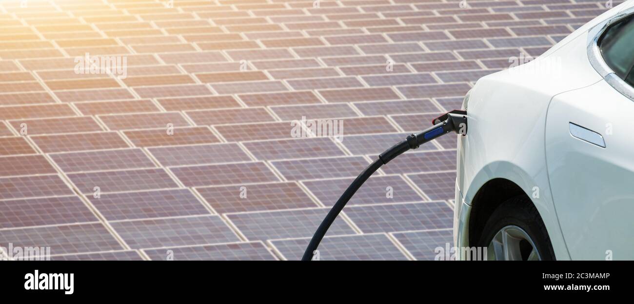 In der Nähe von elektrischen Auto mit angeschlossenem Ladekabel auf dem Hintergrund von Solarzellen und Windräder - Quellen von sauberer, erneuerbarer Energie Stockfoto