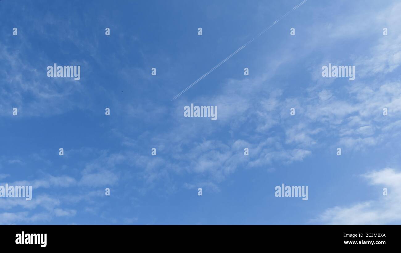 Wolken am blauen Himmel mit Flugzeug und Kondensstreifen, diagonal von oben rechts Stockfoto
