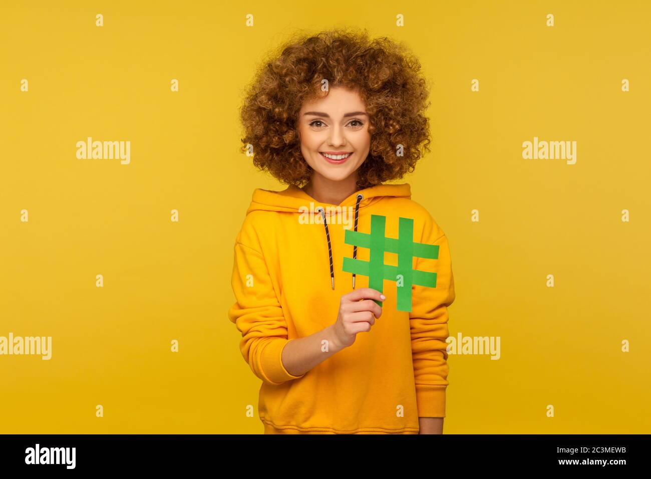 Internet-Trends. Porträt einer glücklichen lockigen Frau im urbanen Stil Hoodie mit großem Hashtag-Zeichen, was Blog-Empfehlung bedeutet, markieren viralen Post. Stockfoto