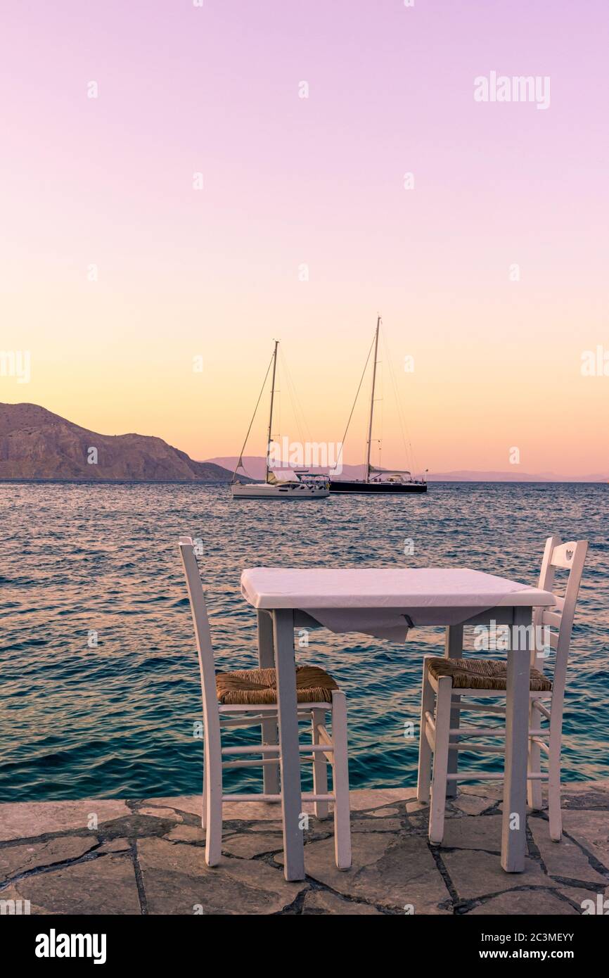 Griechische Ferien vibes mit einem leeren Tisch und Stühlen am Meer auf Symi Insel, Dodekanes, Griechenland Stockfoto