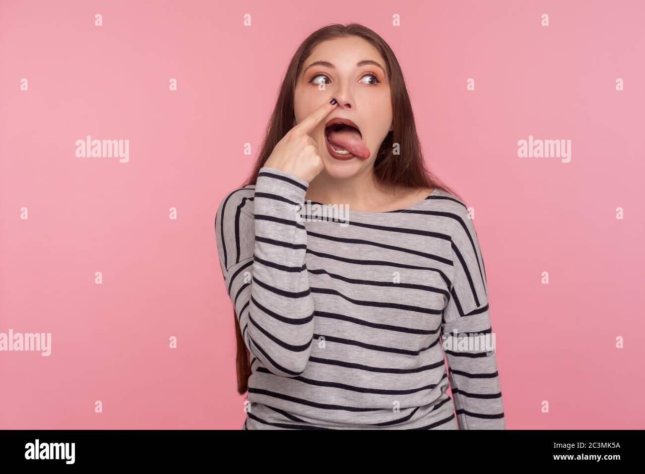 Schlechte Angewohnheit. Portrait von lustigen Frau im gestreiften Sweatshirt Bohren Nase mit humorvollen dummen Ausdruck, macht dumme Grimasse, ragt aus Zunge. ind Stockfoto