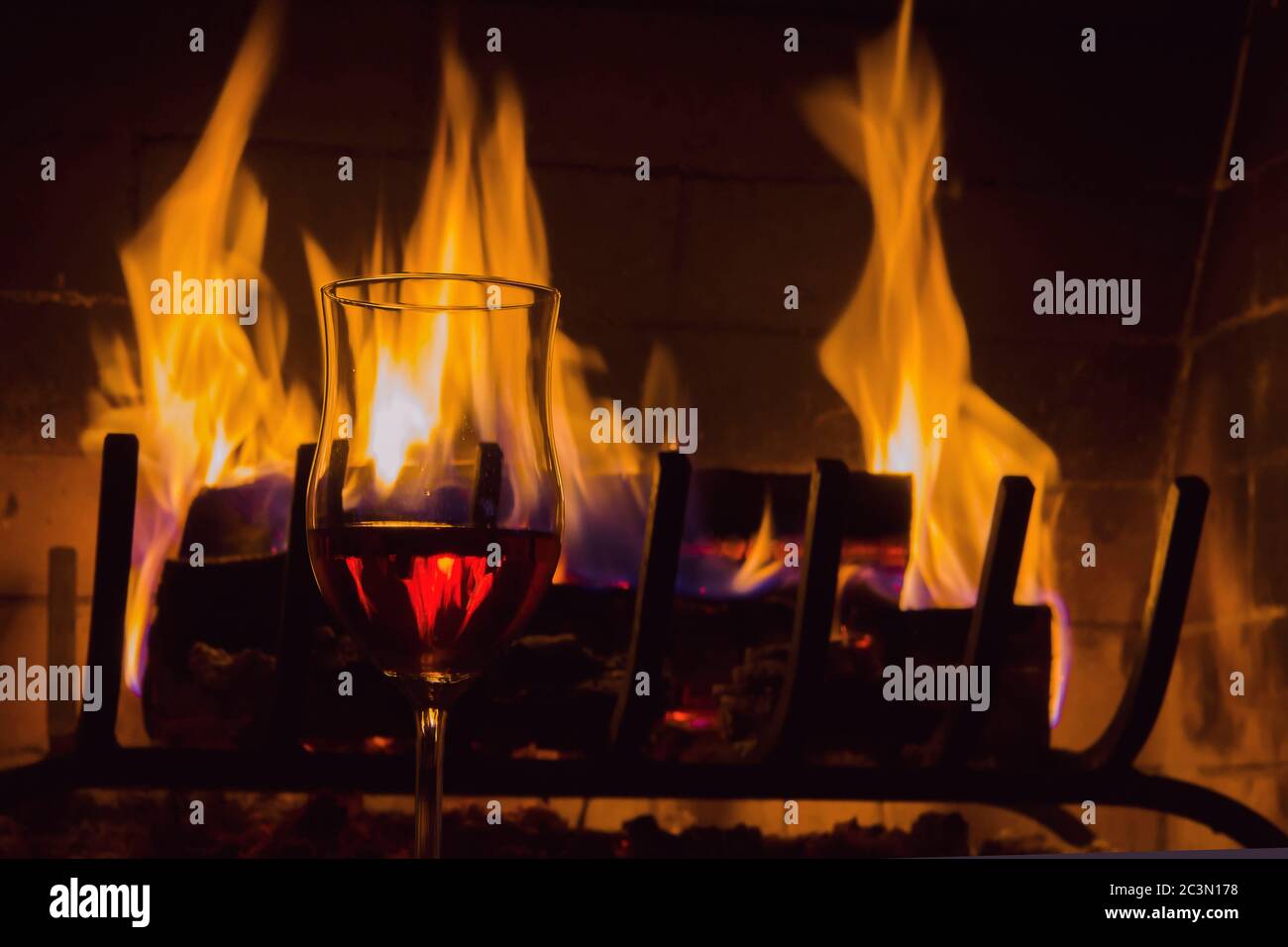 Brennendes Brennholz in einem Kamin, ein Glas Weinstock, helle Flammen, ein Symbol für Wärme und Komfort im Haus Stockfoto