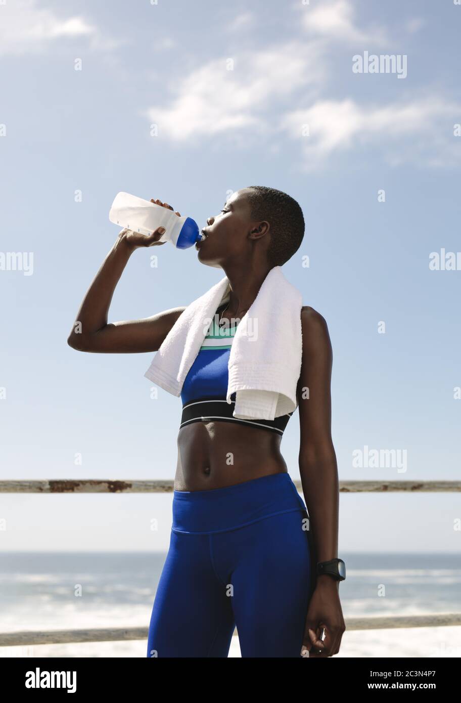 Fit Frau Trinkwasser nach dem Training. Durstige Sportlerin trinkt Wasser im Freien auf der Straße am Meer. Stockfoto