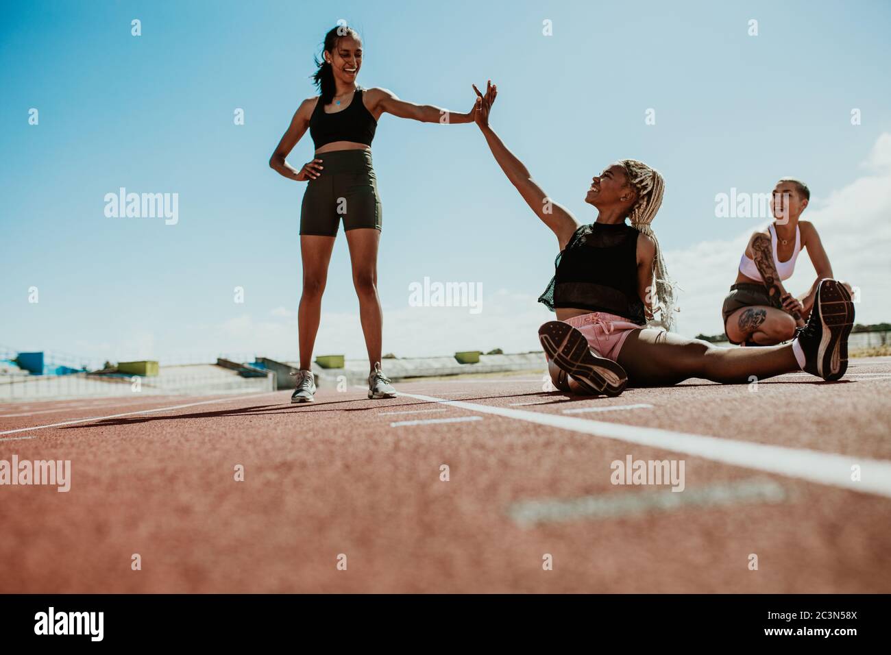 Frauen Athleten, die eine Pause nach dem Training sitzen auf der Laufstrecke und geben High Five im Stadion. Gruppe von drei Sprintern entspannen auf rac Stockfoto