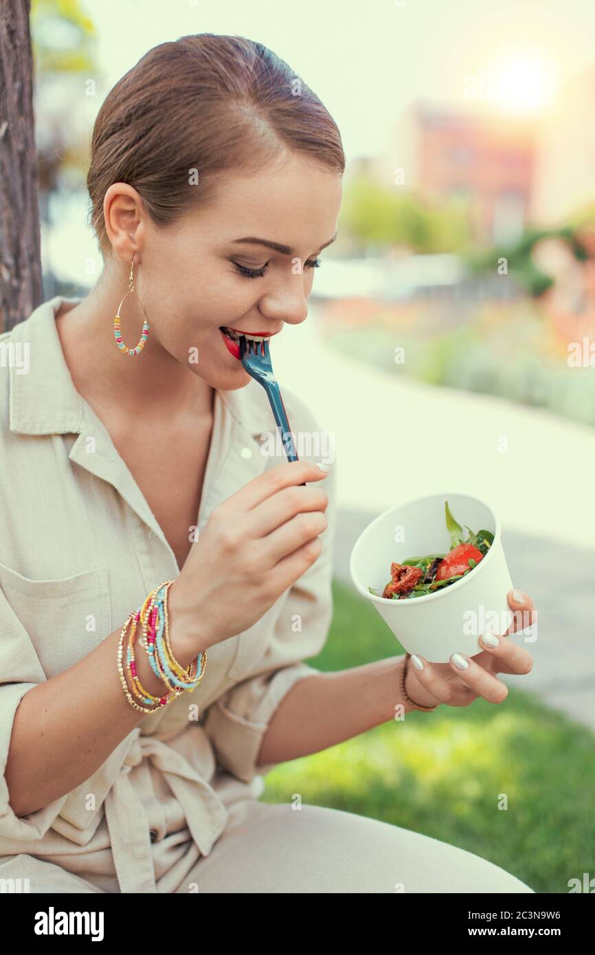 Junge fröhliche Latina Frau essen Salat im Park Stockfoto