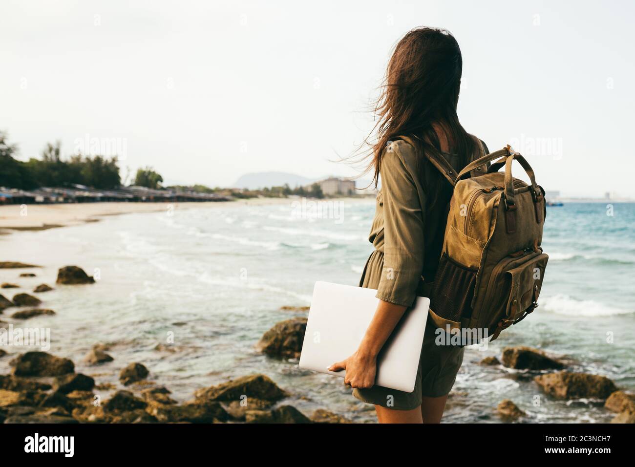 Ein Blick von der Rückseite eines Mädchens auf eine felsige Küste, ein Reisender. Freiberuflicher Arbeiter mit einem Rucksack auf den Schultern und einem Laptop in den Händen, Sea Stockfoto