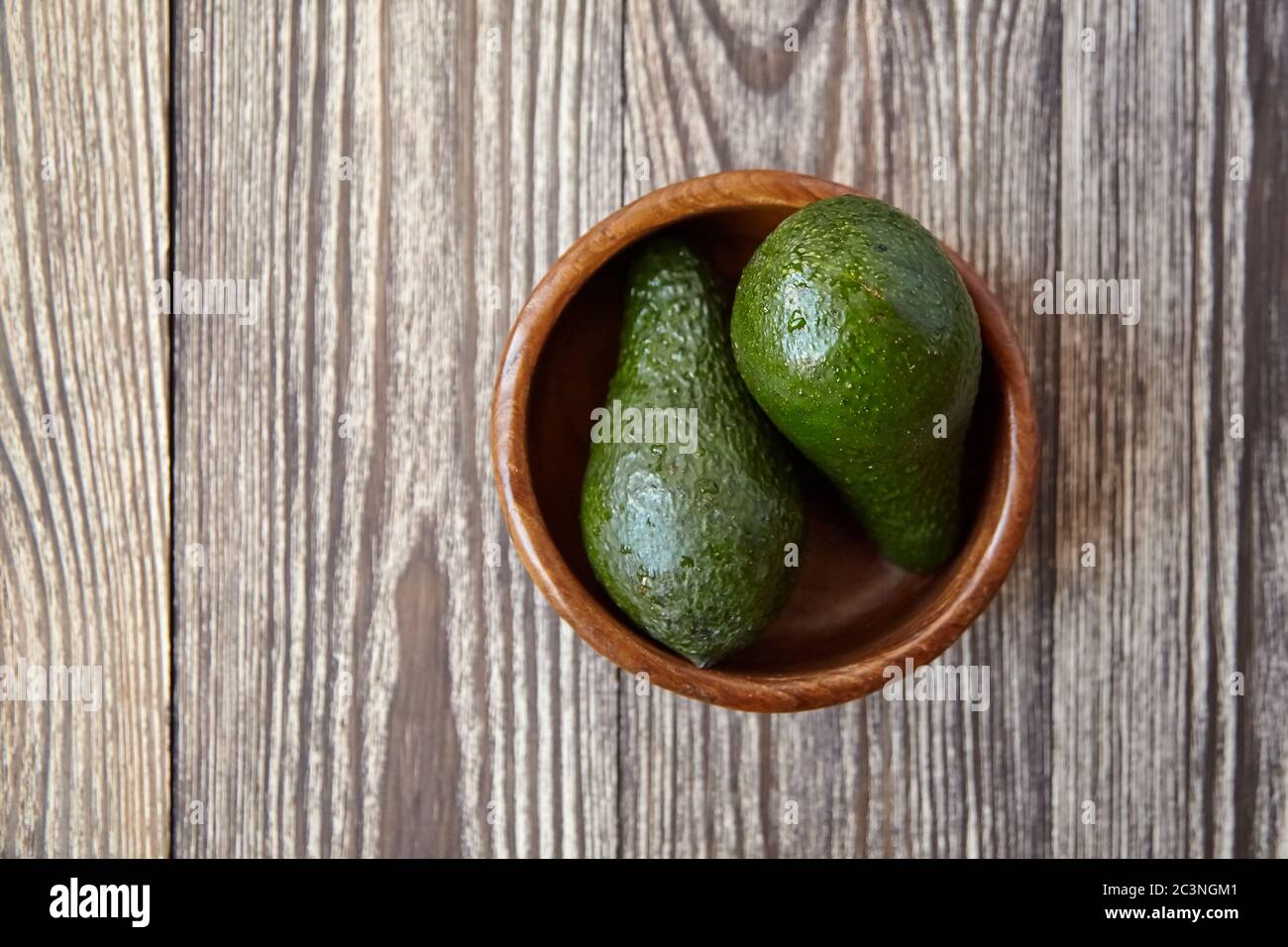 Avocados in einer Schüssel auf Holzhintergrund. Ganz grüne frische tropische Früchte auf braunem Tisch, Draufsicht Stockfoto