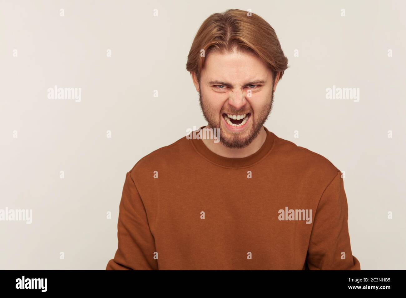 Porträt eines ärgerlichen aggressiven bärtigen Mannes im Sweatshirt, der wild zur Kamera brüllt, starke Wut Irritation ausdrückt, verrückt schreit und voller Hass Stockfoto