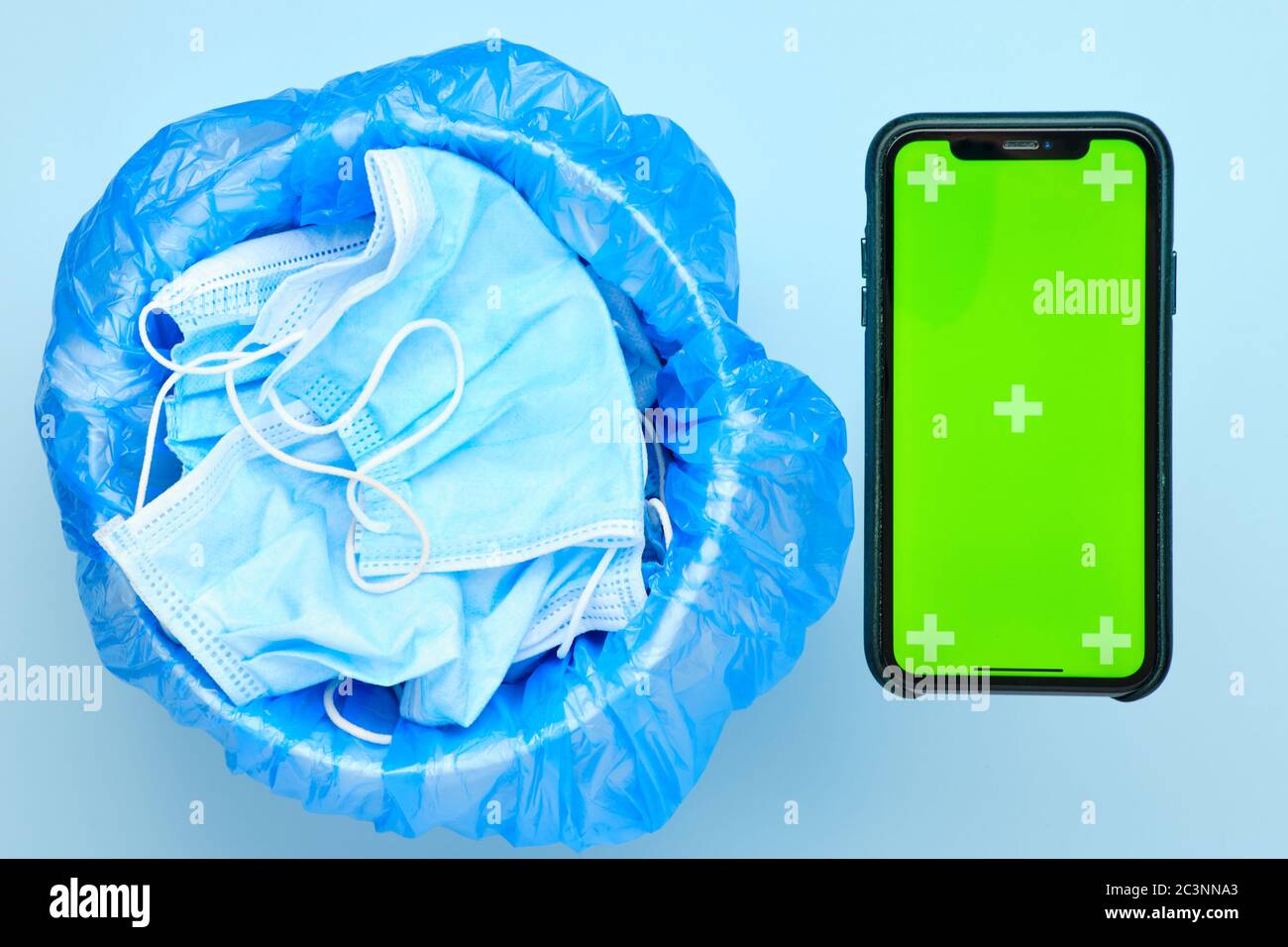 Einweg-OP-Maske in einem Papierkorb und Smartphone mit Chroma-Taste auf blauem Hintergrund. Anwendung des Smart Quarantäne-Konzepts. Stockfoto