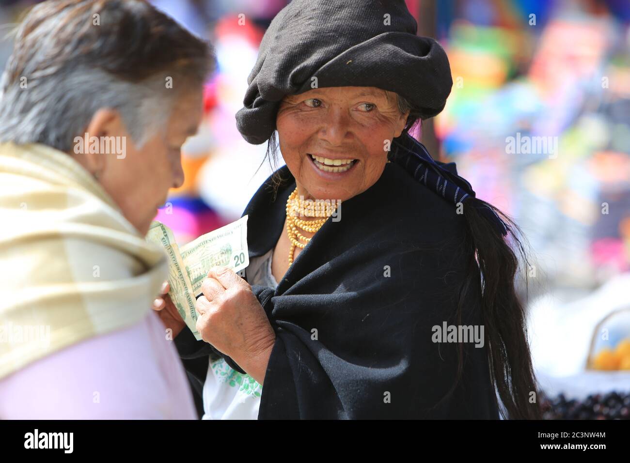 Ältere indigene Frau lächelt, während sie einen Haufen US-Dollar-Scheine auf dem Otavalo-Markt in Ecuador zählt. Stockfoto