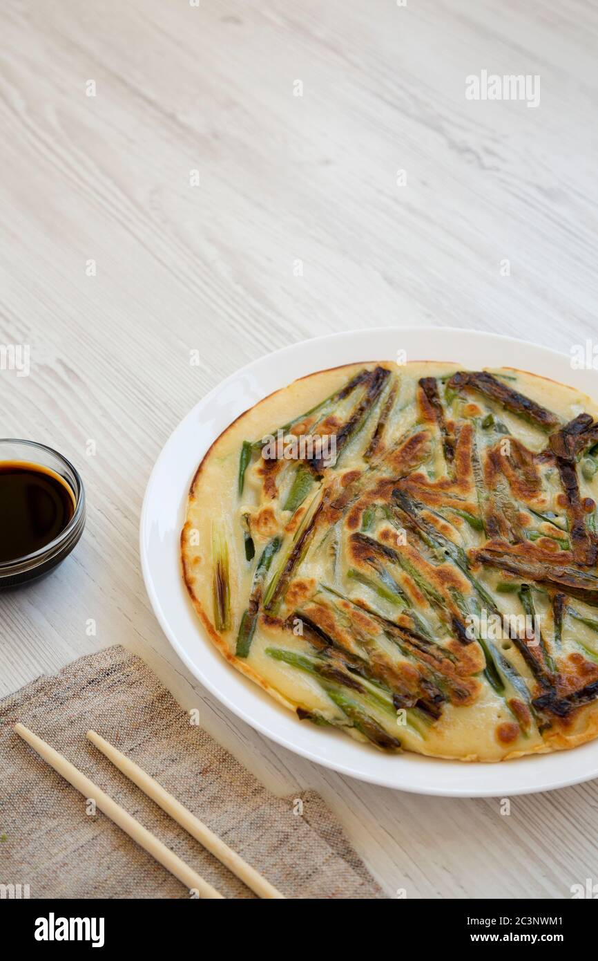 Hausgemachter koreanischer Pajeon-Frühlingszwiebel-Pfannkuchen auf einem weißen Teller auf einer weißen Holzfläche, Seitenansicht. Asiatische Küche. Stockfoto