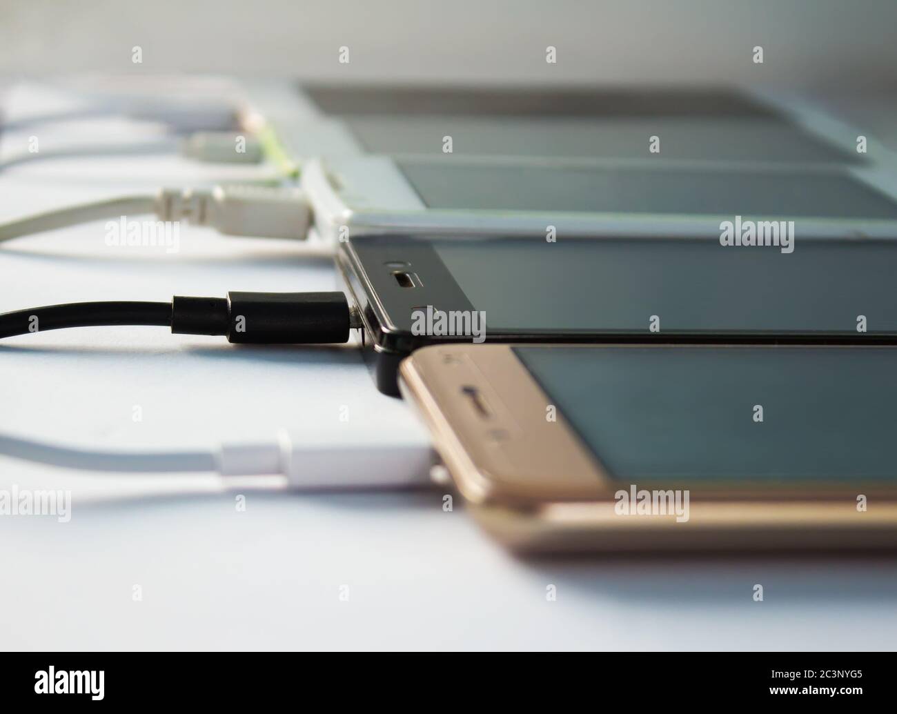 Viele Smartphones auf weißem Hintergrund mit Kabeln aufladen Stockfoto