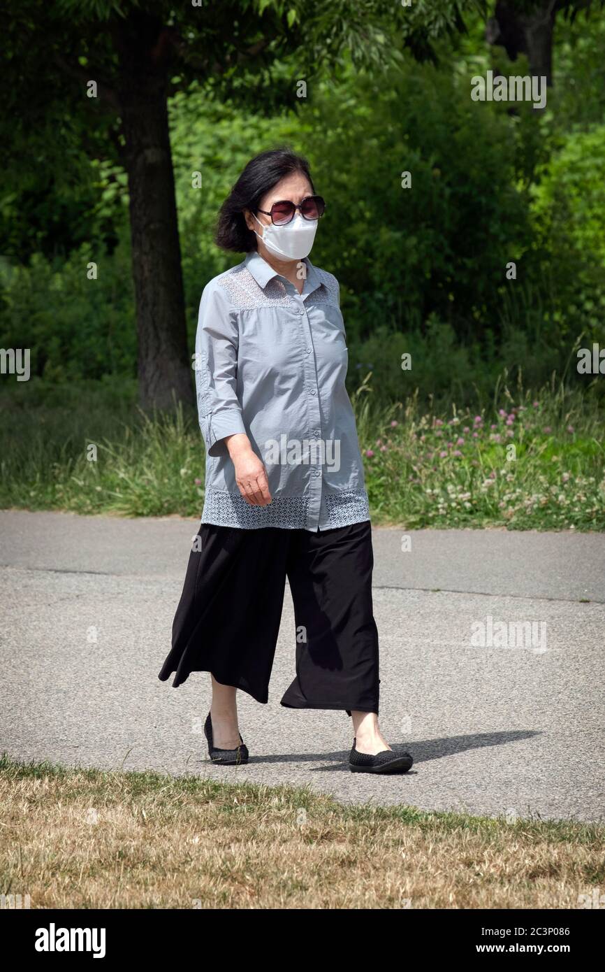Eine stilvoll gekleidete asiatisch-amerikanische Frau mit einer OP-Maske geht auf einen Übungsweg in Little Bay Park in Whitestone, Queens, N.. Stockfoto