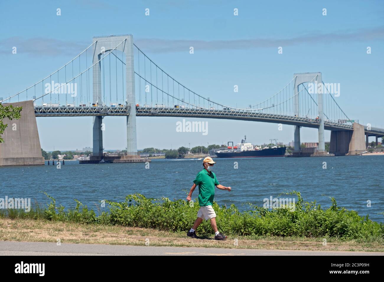 Im Schatten der Throgs Neck Bridge führt ein Mann mit einer OP-Maske einen Pfad in Little Bay Park in Whitestone Queens, New York, durch. Stockfoto