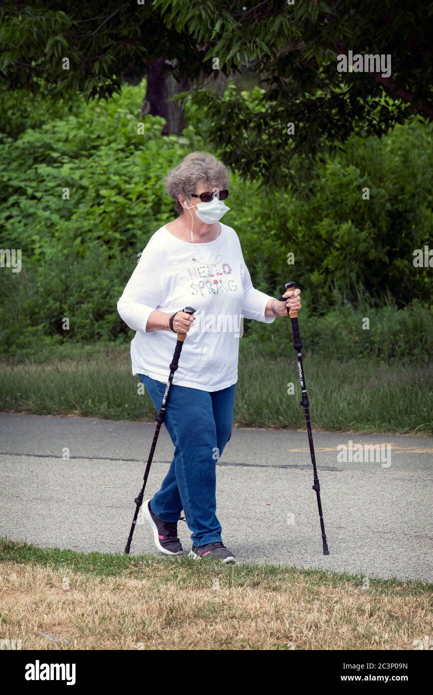 Eine Frau mittleren Alters, die mit Gehstöcken und einer chirurgischen Maske unterwegs ist, um eine Übungswanderung zu machen. In Little Bay Park, Whitestone, Queens, New York City. Stockfoto
