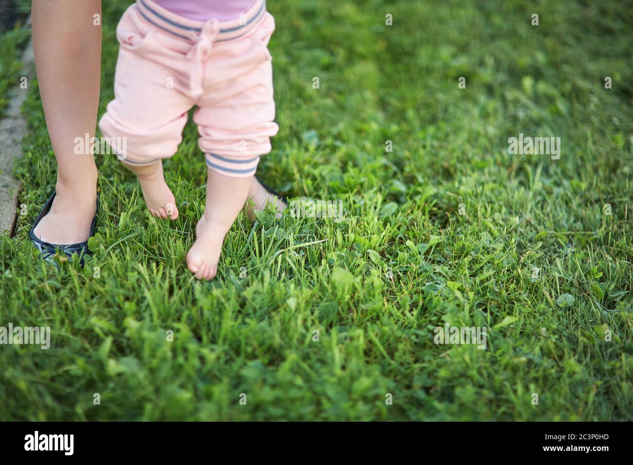 Mutter lehrt ihr Baby, die ersten Schritte barfuß auf dem Gras zu machen. Stockfoto