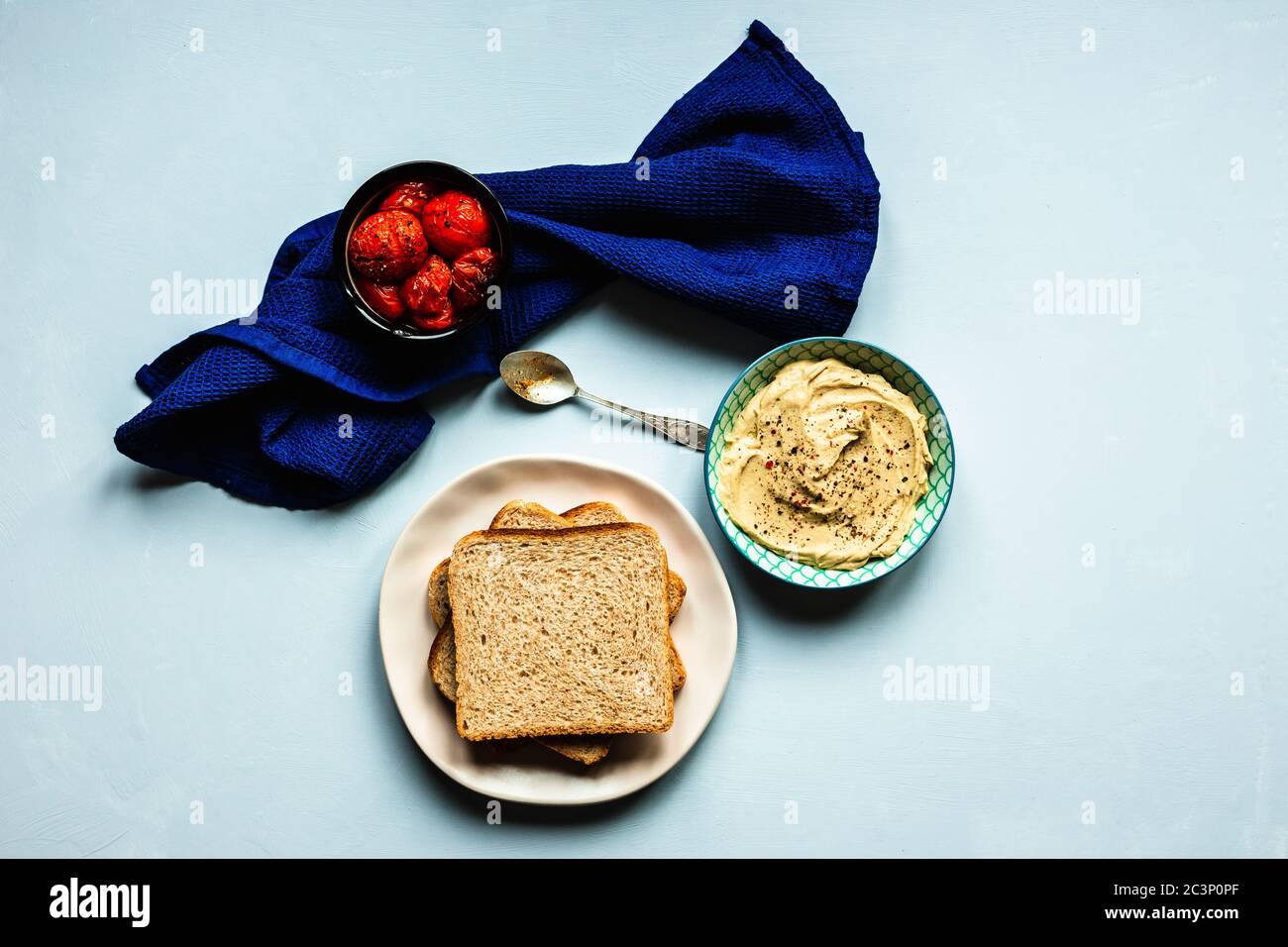 Gebackene Tomaten, Hummus und Brot. Ein tiefblaues Handtuch und ein Löffel. Blauer Hintergrund. Horizontales Bild von oben. Stockfoto