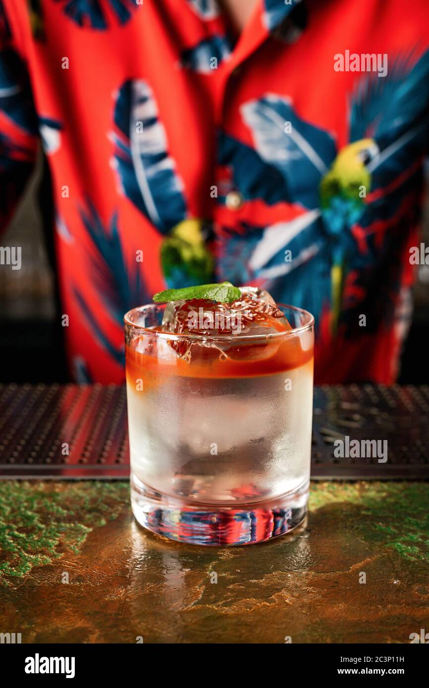 Ein farbenfroher, mehrschichtiger Cocktail im Tiki-Stil in einem Steinglas mit kristallklarem Eiswürfel, garniert mit einem Minzblatt Stockfoto