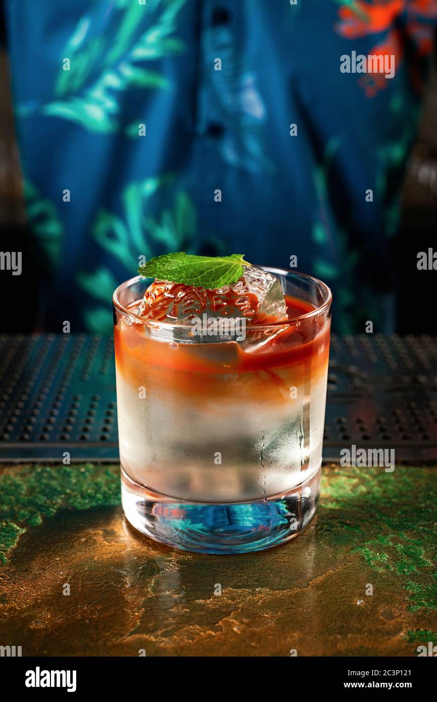 Ein farbenfroher, mehrschichtiger Cocktail im Tiki-Stil in einem Steinglas mit kristallklarem Eiswürfel, garniert mit einem Minzblatt Stockfoto