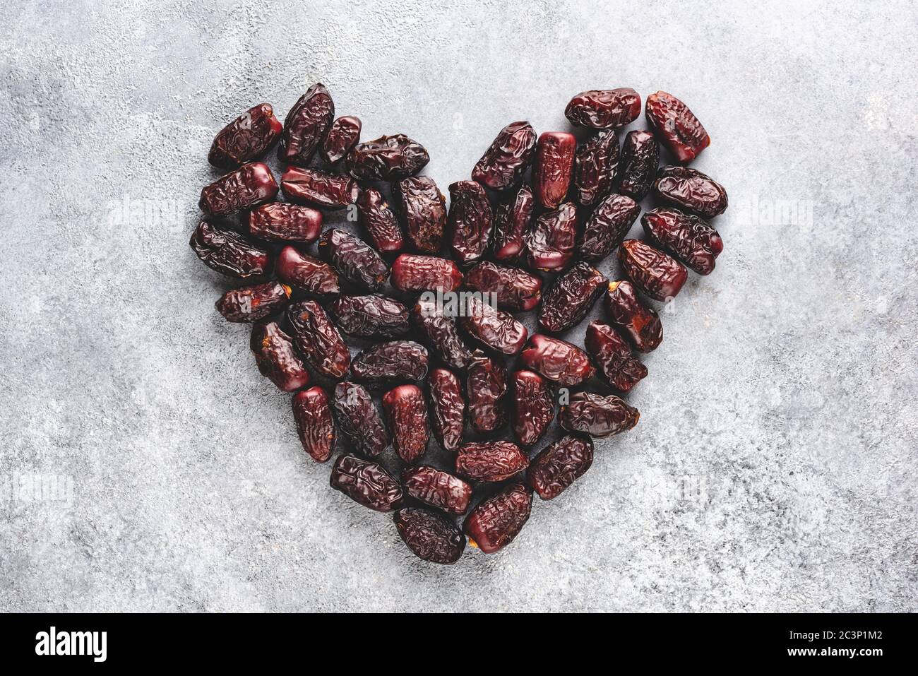 Getrocknete Dattefrüchte auf betonem Hintergrund in Form von Herz. Gesunde arabische vegetarische Speisen Stockfoto