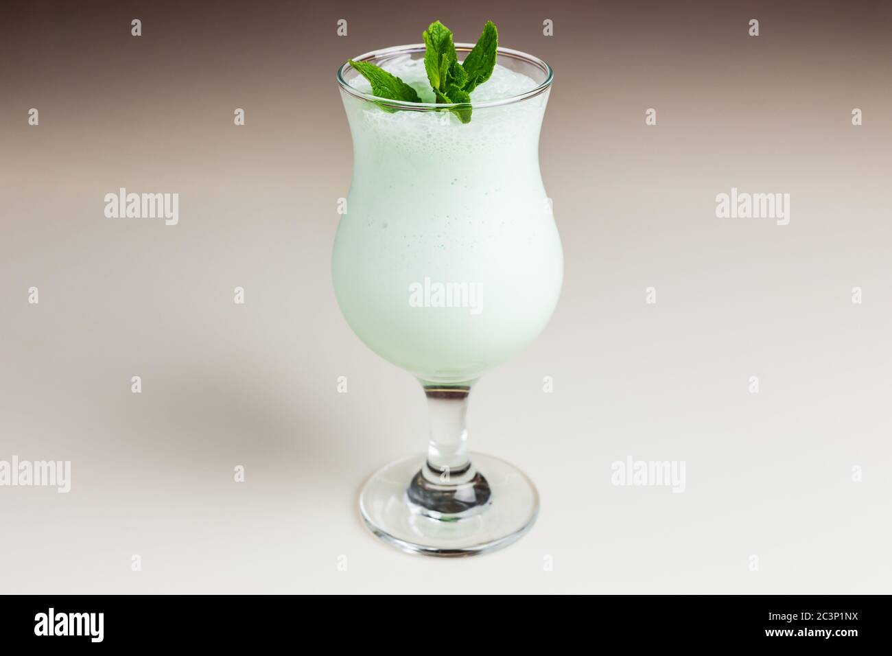 Ein leuchtend grüner Milchshake in einem Hurricane Glas garniert mit einem Minzzweig Stockfoto
