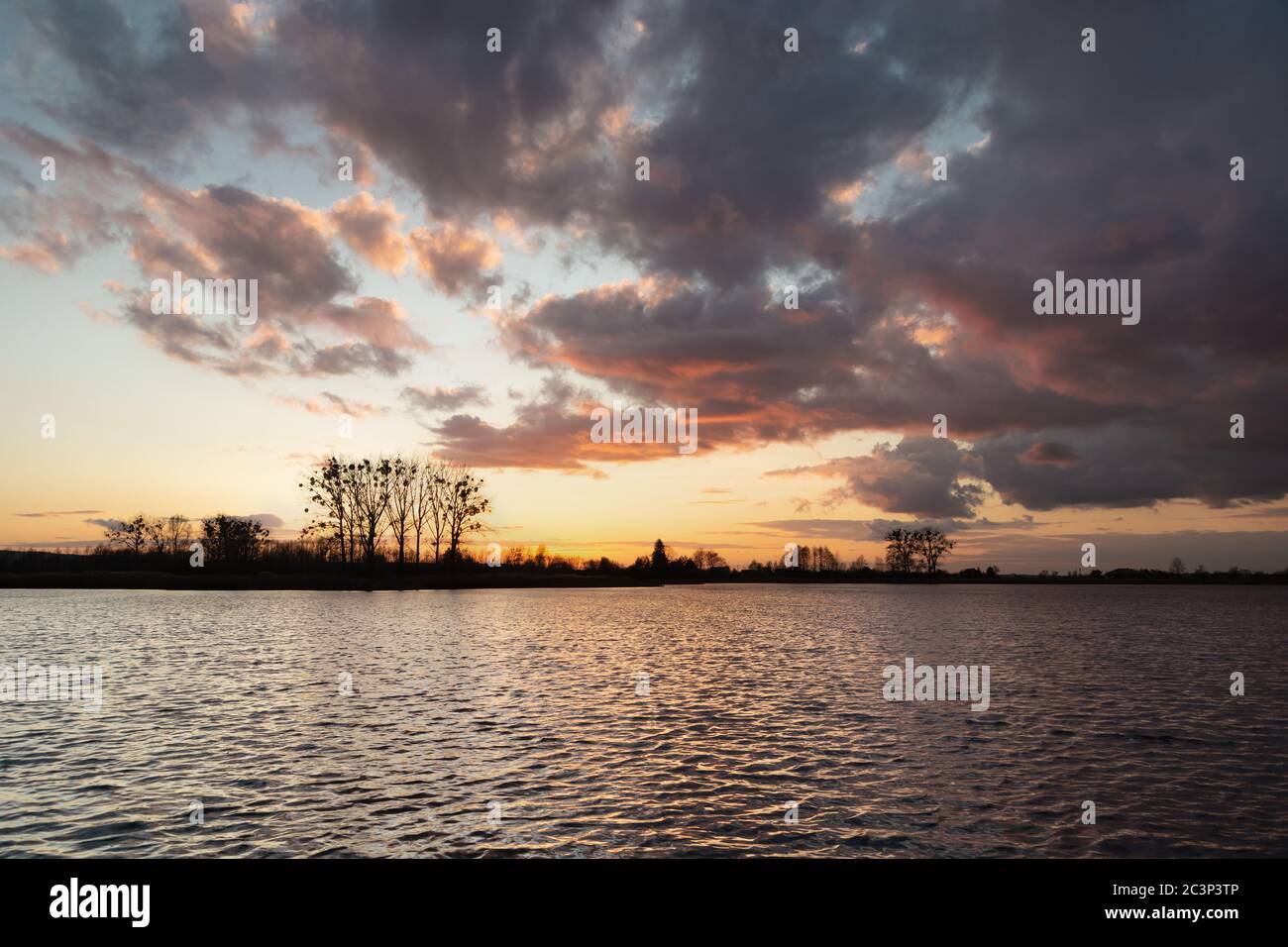 Dunkle Wolken nach Sonnenuntergang auf einem ruhigen See, blick auf den märzabend Stockfoto