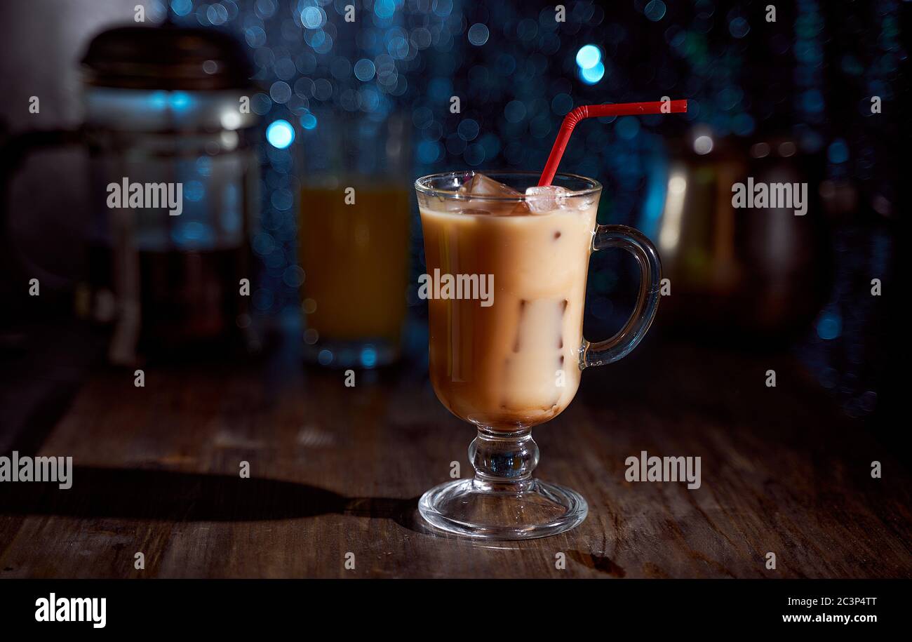 Eiskaffee in einem Latte-Glas mit übergossenem Sahne, Eiswürfeln und Bohnen auf einem alten rustikalen Holztisch. Auf einem dunkelblauen Bokeh-Hintergrund mit Kopierfläche. Stockfoto