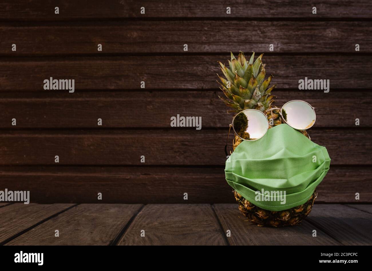 Kühle Ananas mit Sonnenbrille und Gesichtsmaske auf dunklem Holzhintergrund Stockfoto