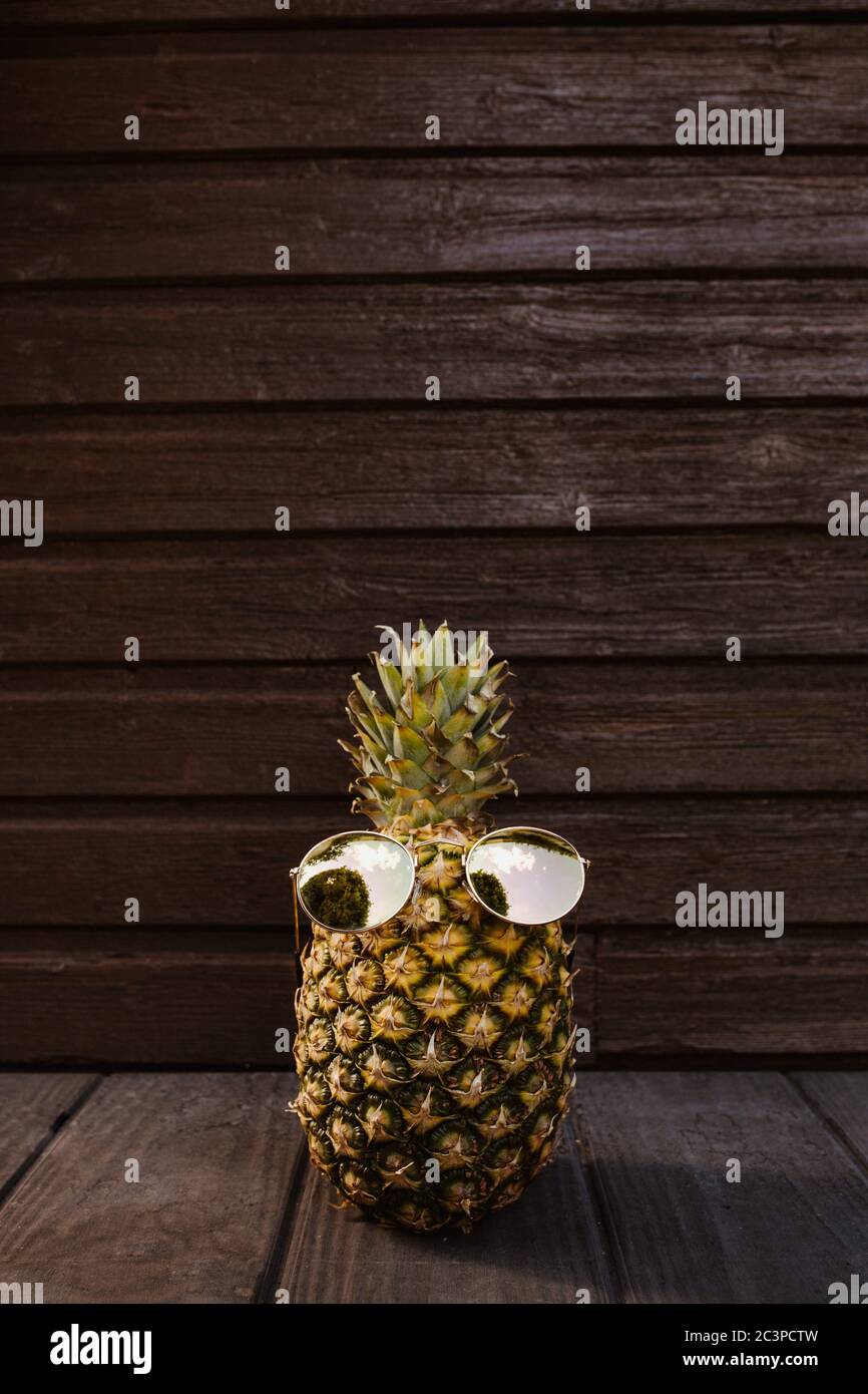 Kühle Ananas mit Sonnenbrille auf dunklem Holzhintergrund Stockfoto