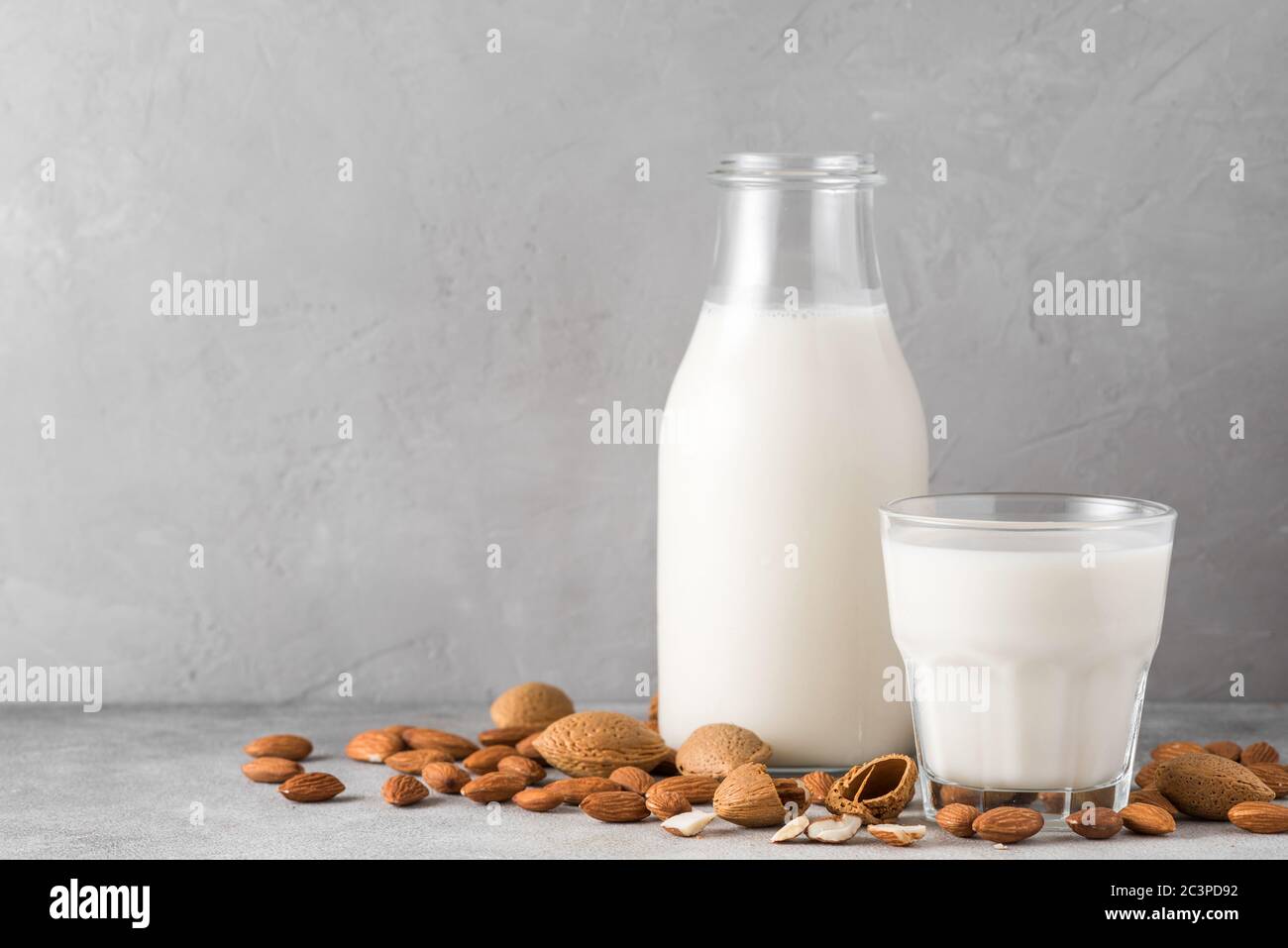 Mandelmilch in einer Flasche mit Glas und Mandelnüssen auf Betongrund. Vegane milchfreie Pflanzenmilch. Nahaufnahme Stockfoto