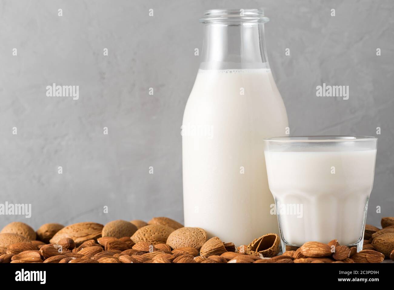 Pflanzenbasierte vegane Mandelmilch in einer Flasche mit einem Glas Milch und Nüssen auf betontem Hintergrund. Milchmilch. Nahaufnahme Stockfoto